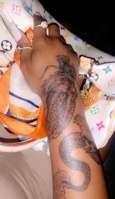 a woman's arm with a dragon tattoo on it and a purse behind her