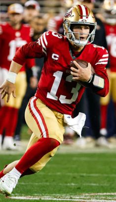 a football player running with the ball in his hand and people watching from the stands behind him