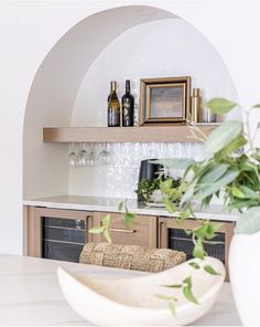 a white vase with some plants in it on top of a counter next to bottles and glasses