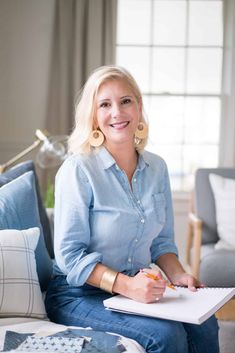 a woman sitting on a couch with a notebook and pen in her hand, smiling at the camera