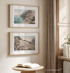 two framed pictures hang on the wall above a table with an open book in front of it