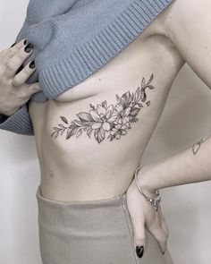 a woman with a flower tattoo on her stomach is holding her hand up to her chest