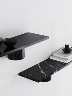 a black shelf with a candle and some books on it next to a white wall