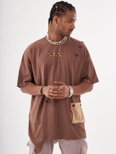 This coffee colored baggy T-shirt is the perfect addition to any beatnik's wardrobe! The button design and the asymmetrical hem gives it a stylish edge. The pocket is both functional and stylish, making this T-shirt a must-have for any fashion-savvy individual. FEATURES- Regular Cut- Smooth Feel- Comfort Fit- 95% cotton, 5% lycra SIZE RECOMMENDATIONModel is a regular size Large and he is wearing size Large Brown T-shirt For Fall Streetwear, Brown Cotton T-shirt With Pockets, Relaxed Fit Brown T-shirt With Pockets, Brown Crew Neck Urban Top, Brown Urban Crew Neck Top, Urban Brown Crew Neck Top, Brown Tops With Pockets For Streetwear, Oversized Brown Tops With Pockets, Oversized T-shirt With Side Pockets