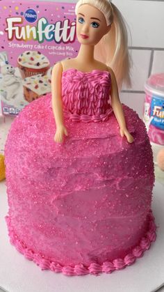 a barbie doll sitting on top of a pink cake with frosting and sprinkles