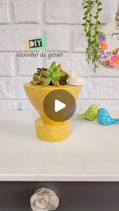 a yellow vase with succulents sitting on top of a white table next to two small birds