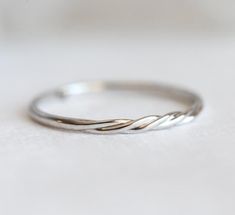 a white gold wedding band with twisted design on the top and bottom, sitting on a table