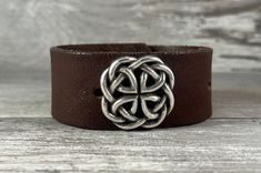 Silver tone Celtic knot on a distressed brown genuine leather strap upcycled from an old belt. This handcrafted cuff bracelet features some gorgeous markings that give this piece great character! See photos for views that show these markings. This would make a great gift for anyone with proud Irish heritage, or heck, anyone who WISHES they had proud Irish heritage! SIZING: The bracelet is adjustable with two snaps, and will fit a 7" wrist. Not sure what size your wrist is? Check out this free pr Rustic Brown Cuff Bracelet As Gift, Rustic Leather Bracelet With Patina As Gift, Rustic Leather Bracelet With Patina For Gift, Rustic Brown Cuff Bracelet Gift, Handmade Vintage Brown Leather Bracelet, Vintage Brown Leather Bracelet With Waxed Finish, Brown Leather Bracelet With Patina, Adjustable Brown Cuff Bracelet With Patina, Adjustable Brown Leather Bracelet With Patina