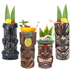 three tiki style vases with fruit and drinks in them, one is made out of wood