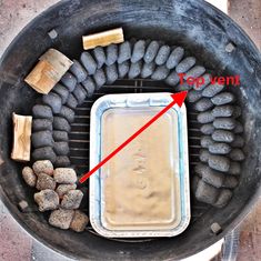 an outdoor grill with rocks and food cooking on it's side as well as a red arrow pointing to the top vent