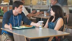 a man and woman sitting at a table with food in front of them, talking to each other