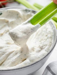 a person dipping dip into a bowl with celery sticks