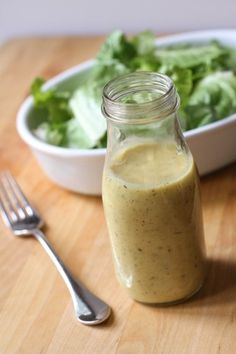 a glass jar filled with dressing next to a bowl of lettuce and a fork