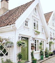 a row of white houses with green doors, windows and plants on the side of them