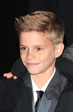 a young boy in a suit and tie posing for the camera with his arm around him