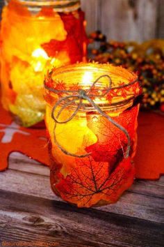 two mason jars filled with autumn leaves on top of a wooden table