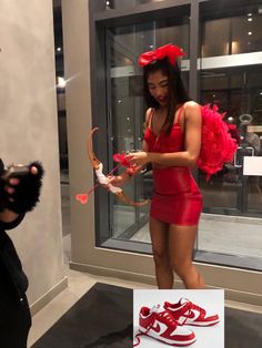 a woman in a red dress is holding a bow and looking at her cell phone