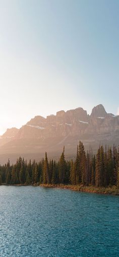 there is a boat on the water near some trees and mountains in the back ground