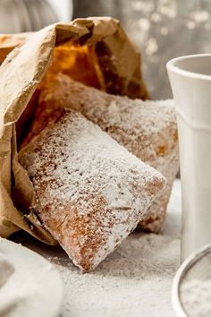 powdered sugar on top of two pieces of bread next to a cup and saucer