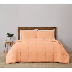 a bed with an orange comforter on top of it and a plant in the corner