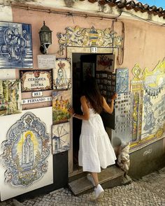 a woman in a white dress standing at the door to a building with many tiles on it