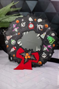 a black wreath decorated with halloween stickers and a red bow on a white table