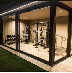 an indoor gym with exercise equipment in the glass walls and green grass on the ground