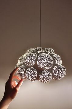 a hand is holding a light fixture in the shape of a cloud with circles on it