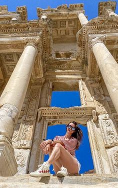 a woman sitting on top of a stone building next to tall white pillars and columns