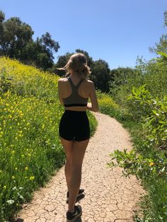 a woman is walking down a dirt path in the middle of wildflowers and trees