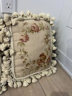 a decorative pillow with tassels and flowers on it sitting next to a light switch