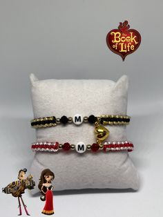 two bracelets are sitting on top of a pillow and one is holding a doll