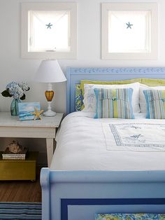 a bedroom with blue and white bedding, two windows and a nightstand in the corner