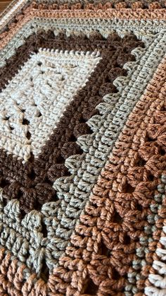 a crocheted blanket is laying on a wooden table with a brown and white pattern