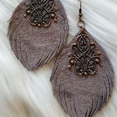 two pairs of brown leather earrings on top of a white fur surface with beads and chains hanging from them