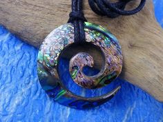 a necklace with a spiral design hanging from a wooden piece on a blue cloth covered surface