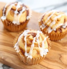 three cupcakes sitting on top of a wooden cutting board with icing drizzled around them