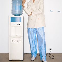 a woman standing next to a water dispenser in front of a white wall