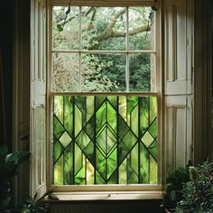 a green stained glass window with plants in the foreground and trees in the background