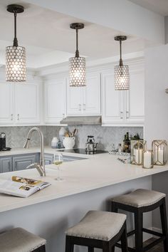 a kitchen with three lights hanging from the ceiling and two stools on the counter