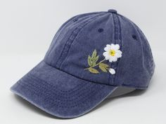 a blue baseball cap with white flowers embroidered on the front and back side, sitting against a white background