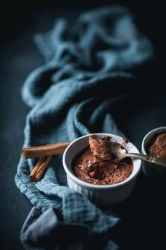 two bowls filled with chocolate pudding on top of a blue cloth next to cinnamon sticks