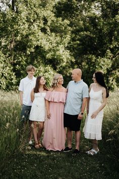 a group of people standing next to each other in the grass with trees behind them