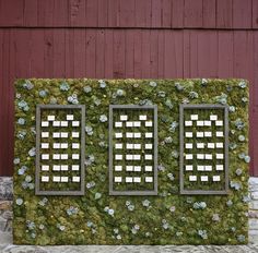 a moss covered wall with three windows on it's sides and flowers all over the side