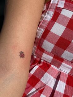 a ladybug tattoo on the arm of a woman in a red and white checkered dress