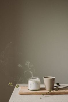 a white cup sitting on top of a table next to a candle and some leaves