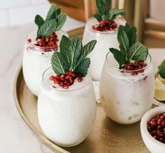 three glasses filled with yogurt and garnish on a gold platter