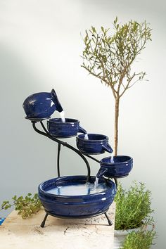 a blue fountain with five bowls on it and a tree in the backgroud