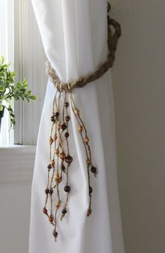 a white curtain with some beads hanging from it's side next to a potted plant