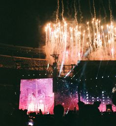 fireworks are lit up in the night sky as people watch from their seats at an outdoor concert